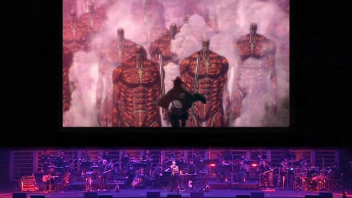 A screenshot from the Attack on Titan Orchestra advertisement. It's a photo from a previous show, with the orchestra on the stage with a vocalist and somebody playing the keyboad, with a large screen above them playing a scene from the show of a Survey Corp member in the air with their ODM gear, approaching an army of Titans.